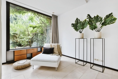 Renter friendly decor may include an ottoman with built-in storage as shown here. Additional ideas include plants and curtains, as shown here by a large window. 